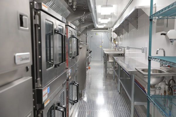 A fully equipped mobile kitchen trailer featuring stainless‑steel ovens, prep counters, and storage racks.