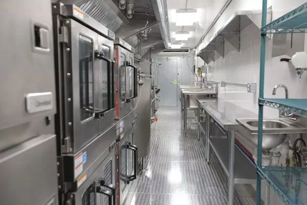 A fully equipped mobile kitchen trailer featuring stainless steel ovens, prep counters, and storage racks