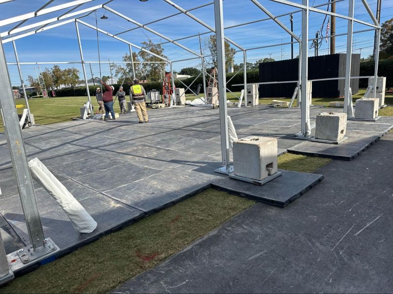 A modular metal frame atop portable flooring with concrete ballast blocks.