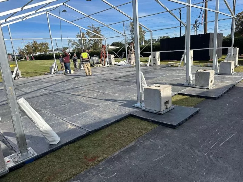 A modular metal frame atop portable flooring with concrete ballast blocks. 