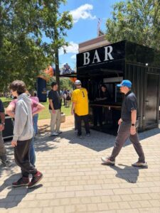 Container bar with a BAR sign and festival guests walking past