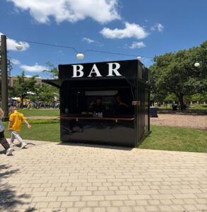 Black shipping container bar with a BAR sign at an outdoor festival