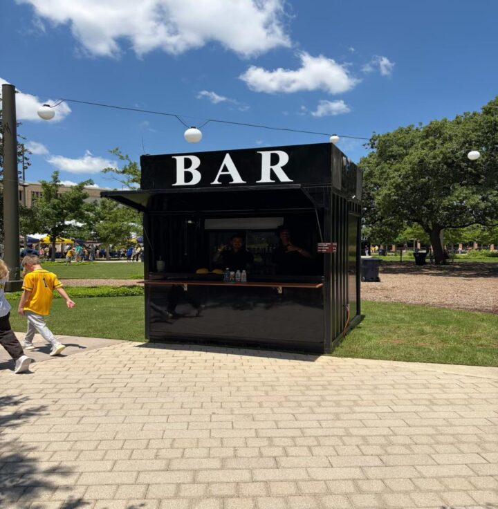 Black shipping container bar with a BAR sign at an outdoor festival