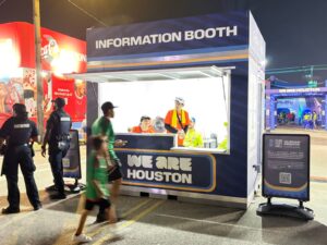 Branded container information booth with staff at a fan zone at night