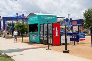 Teal container bar with drink coolers and crowd barriers at an outdoor fan zone